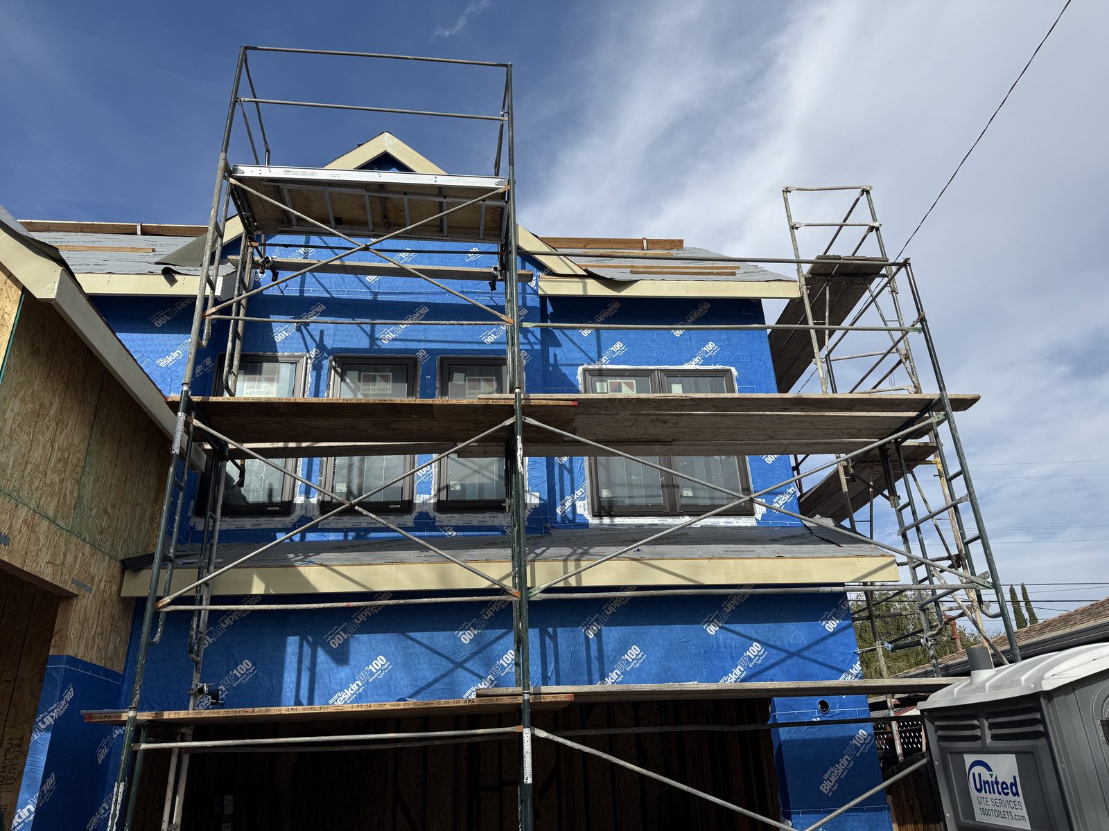 Multi-story home addition in progress with scaffolding and weather wrap